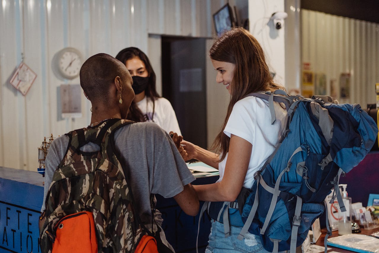 about-me Diverse travelers with backpacks checking in at a lively hostel reception.