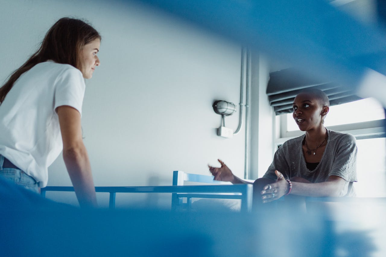 photography-service-01 Two women enjoying a friendly conversation in a hostel room with bunk beds.